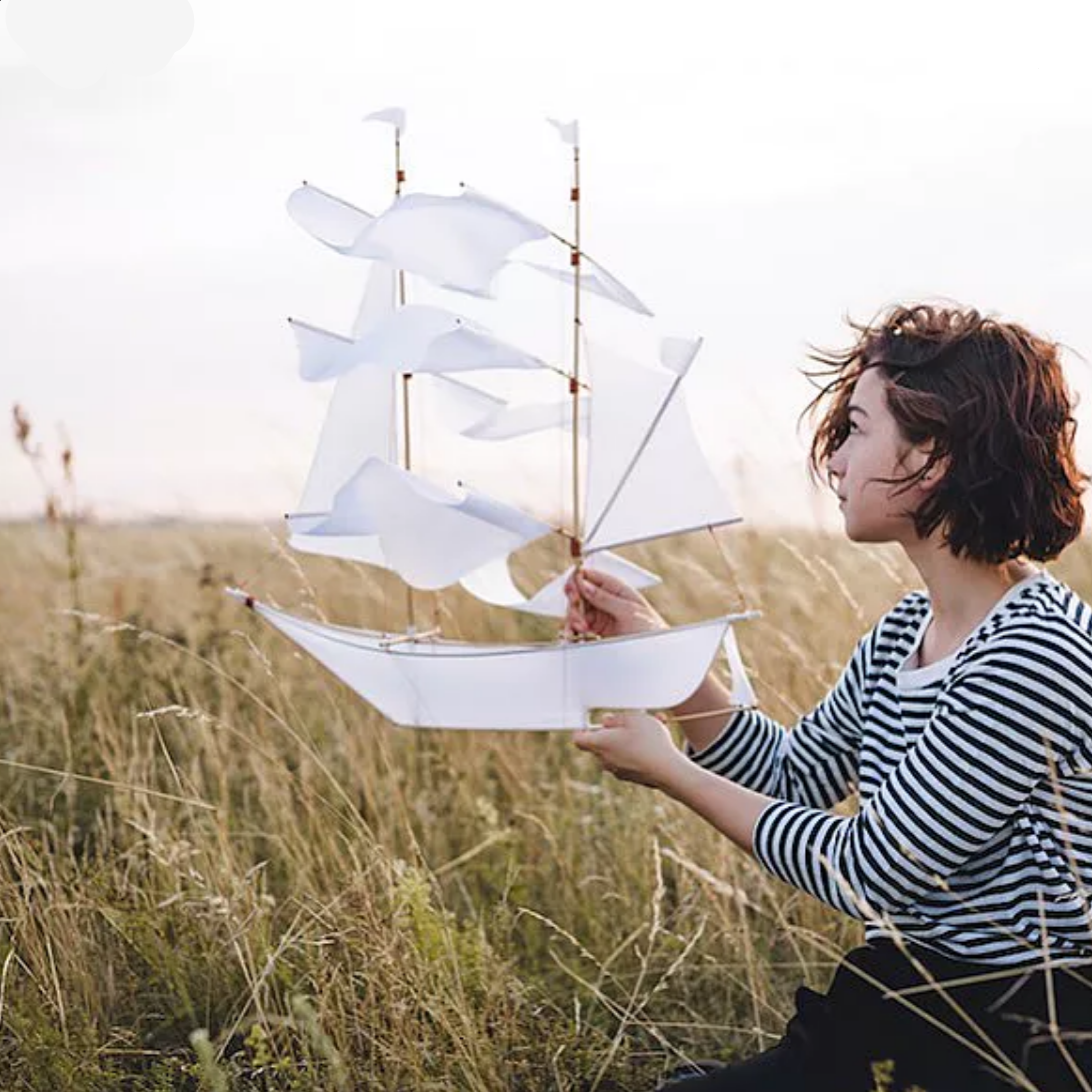 Person holding a large white paper boat in a field