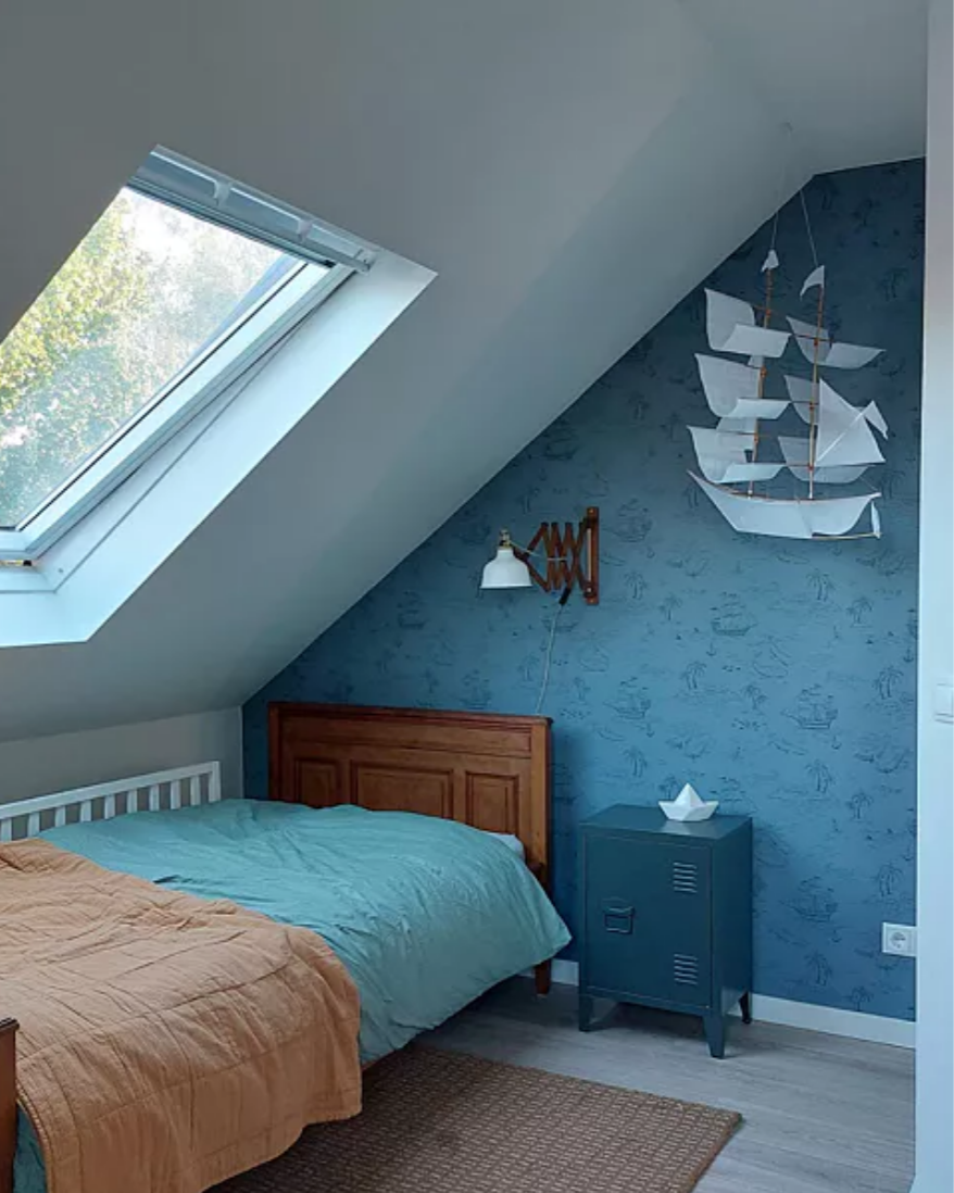 Attic bedroom with blue walls, wooden bed, and decorative ship on the wall.
