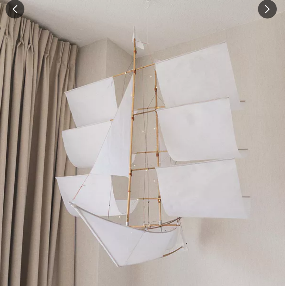 Decorative ship model with white sails against a neutral wall.