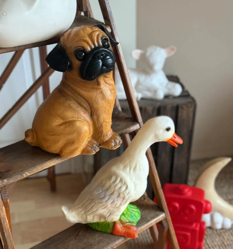 Decorative figurines of a dog and duck on a wooden ladder with a neutral background