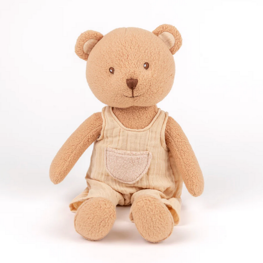 Stuffed teddy bear wearing beige overalls on a white background