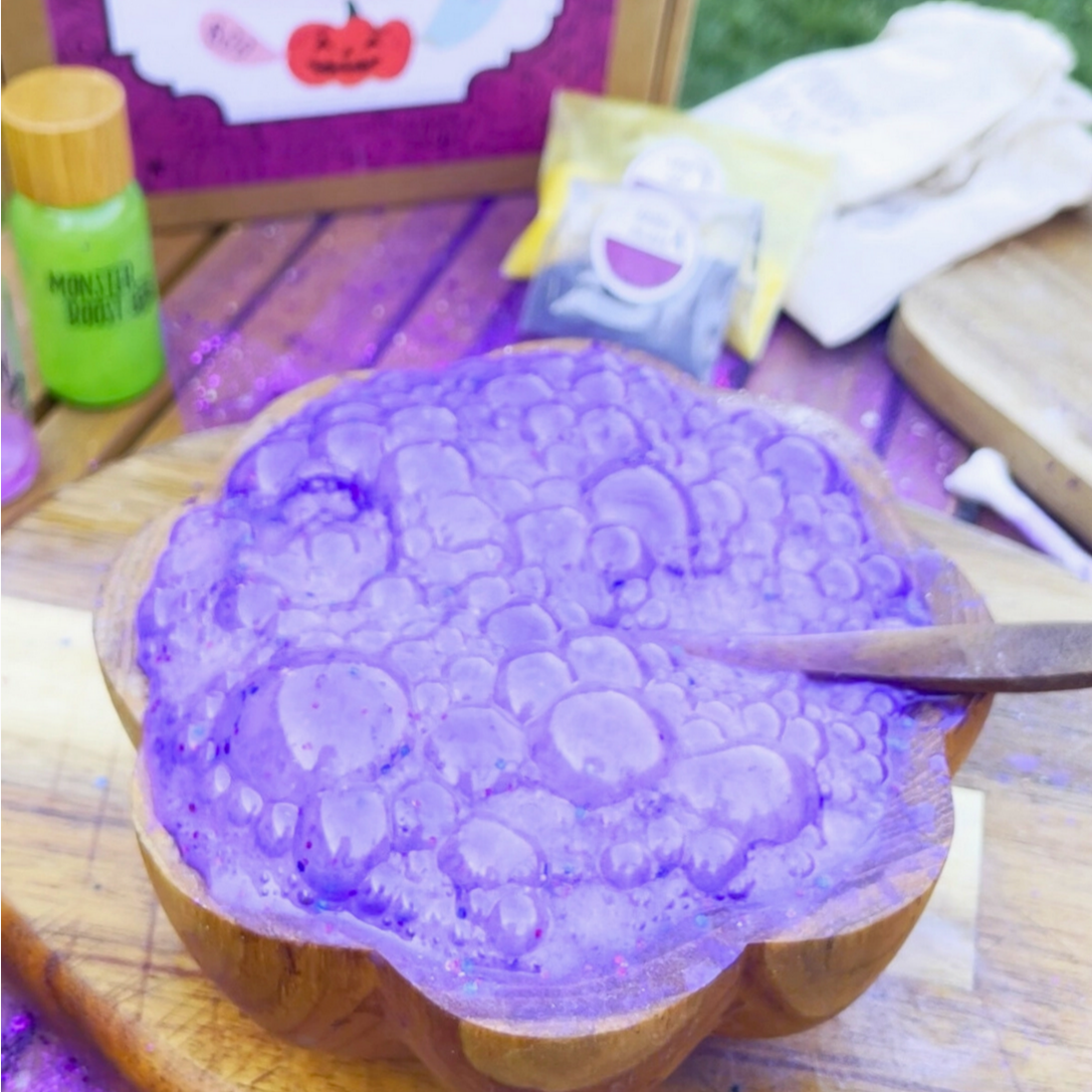 Purple bubble bath in a wooden bowl with a Halloween-themed box in the background.