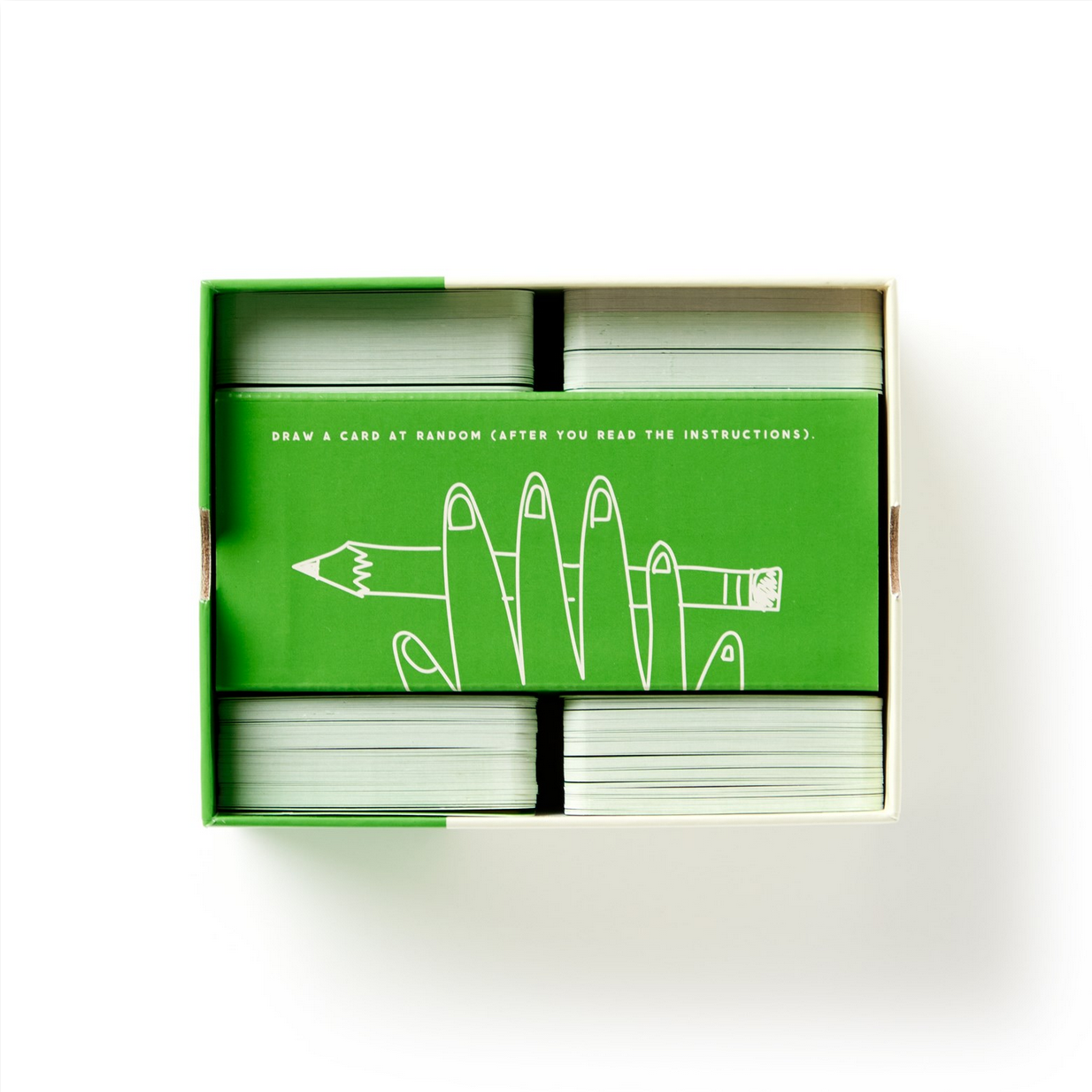Card game box with green top flap featuring a hand holding a pencil illustration on a white background
