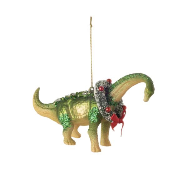 Decorative dinosaur ornament with green glittery texture, red bow, and small tree on a white background.