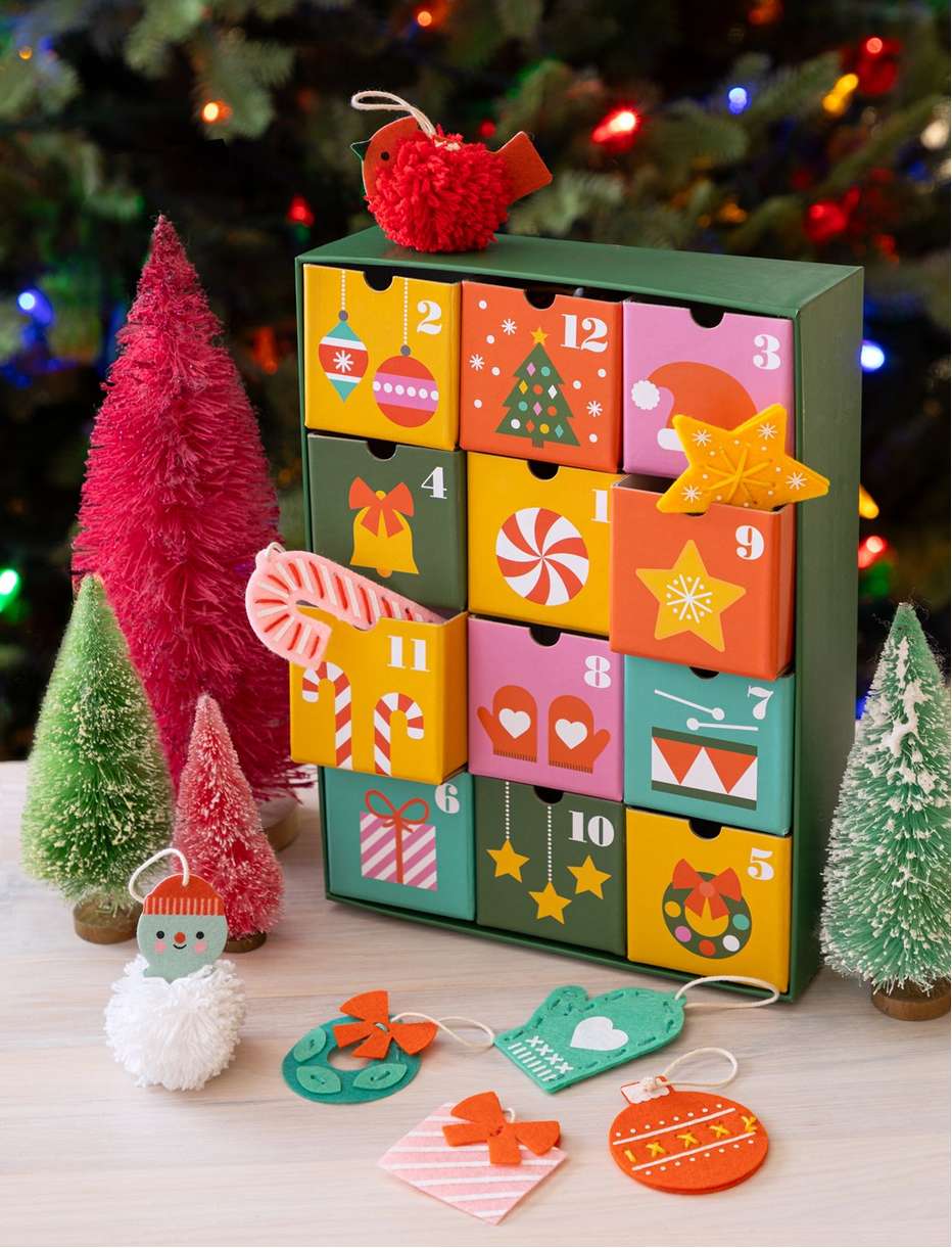 Colorful advent calendar with small doors, Christmas decorations, and trees in the background.