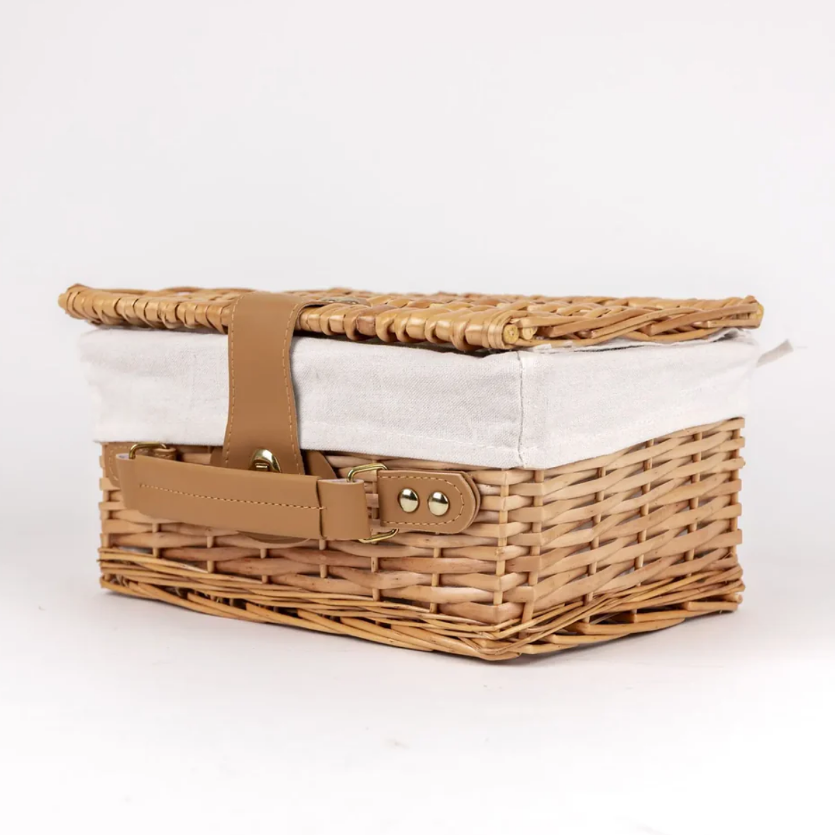 Wicker picnic basket with a white liner and brown handles on a white background