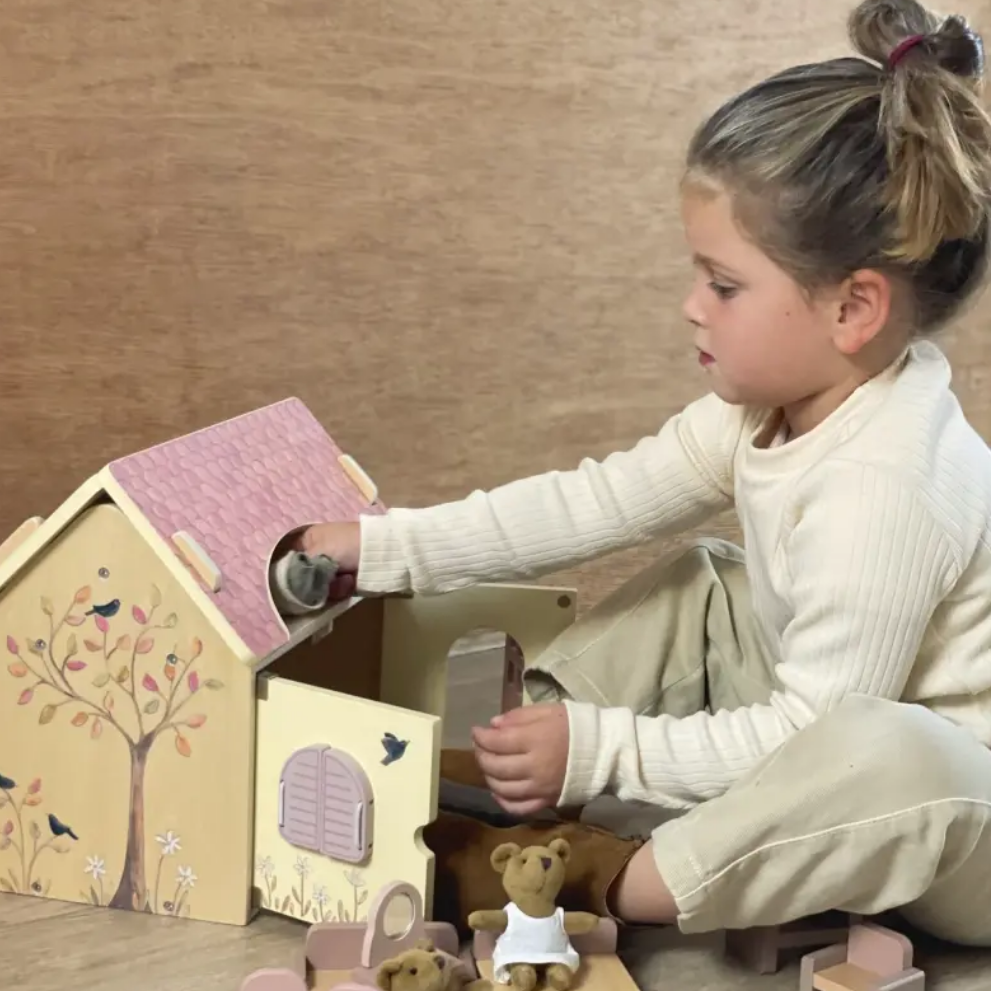 Child playing with a wooden dollhouse and toys on a wooden floor.