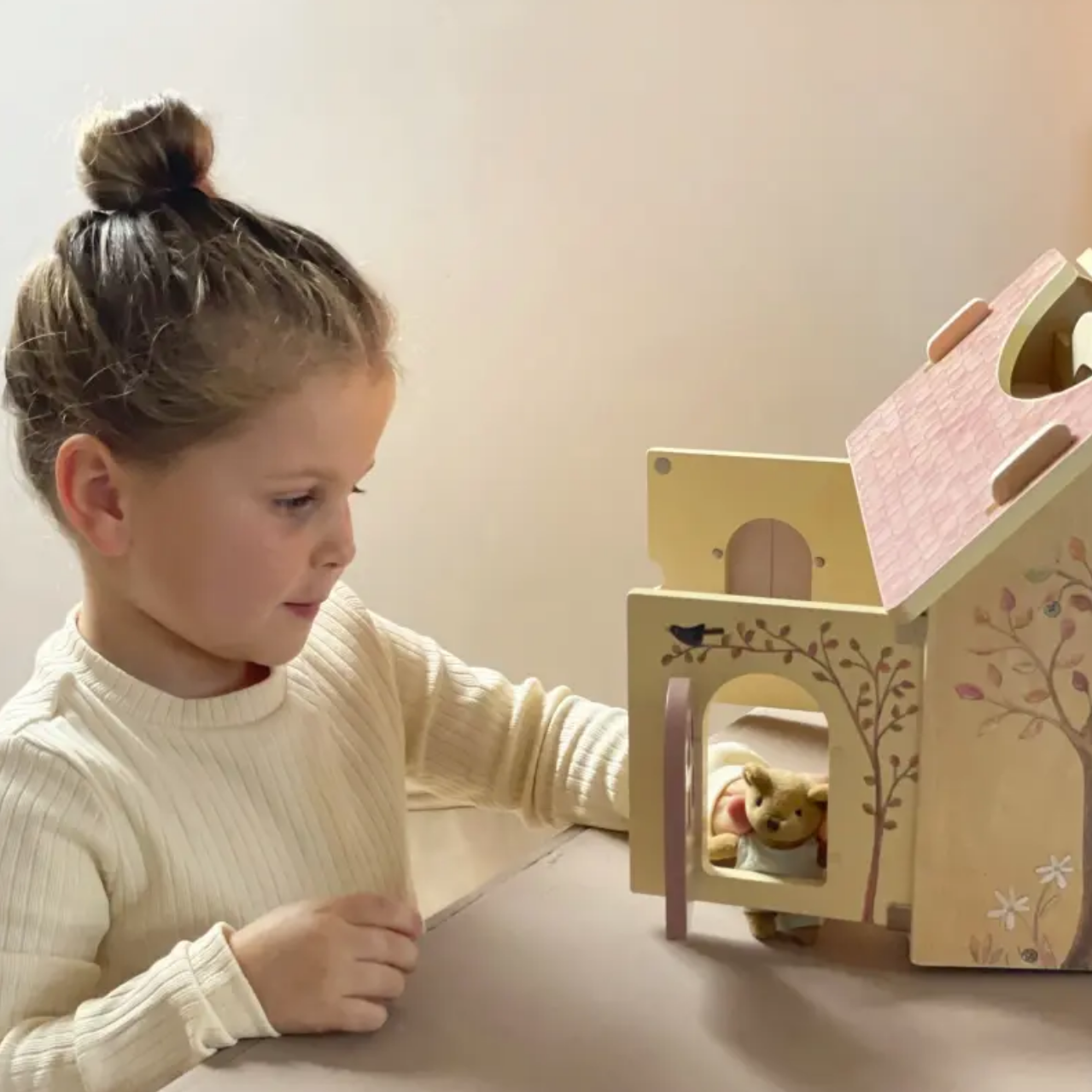Young girl playing with a wooden dollhouse on a light surface.