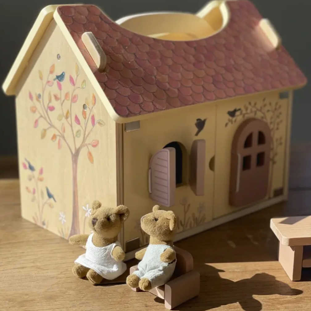 Wooden toy house with two teddy bears in front on a wooden surface.