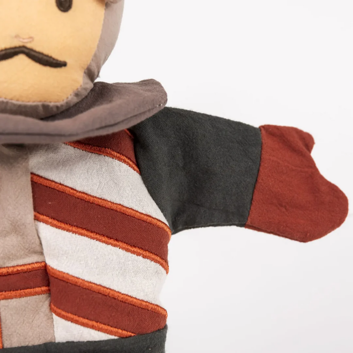 Close-up of a plush puppet resembling a knight with a striped scarf and hood on a white background