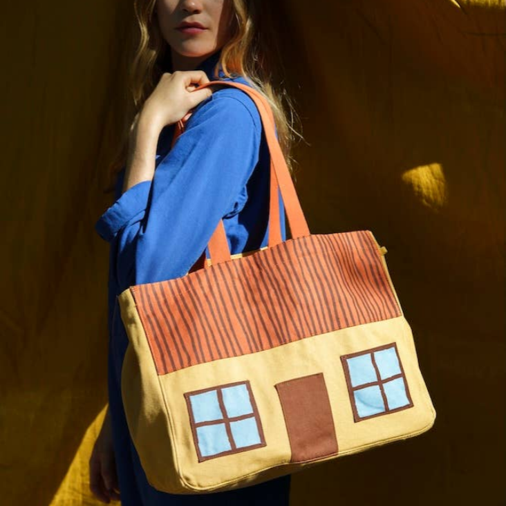 Person holding a house-shaped bag against a warm-toned background