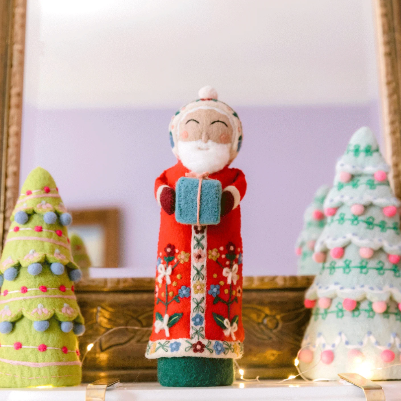 Decorative Christmas figures including a Santa Claus and trees on a mantel.