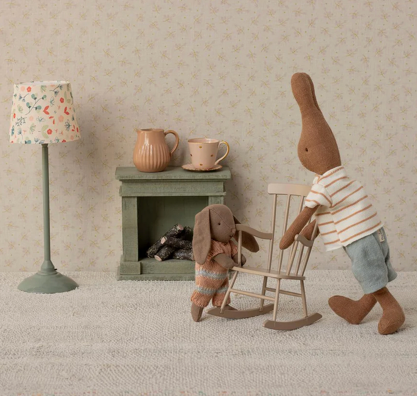 Two toy bunnies in a room with a lamp and small table.