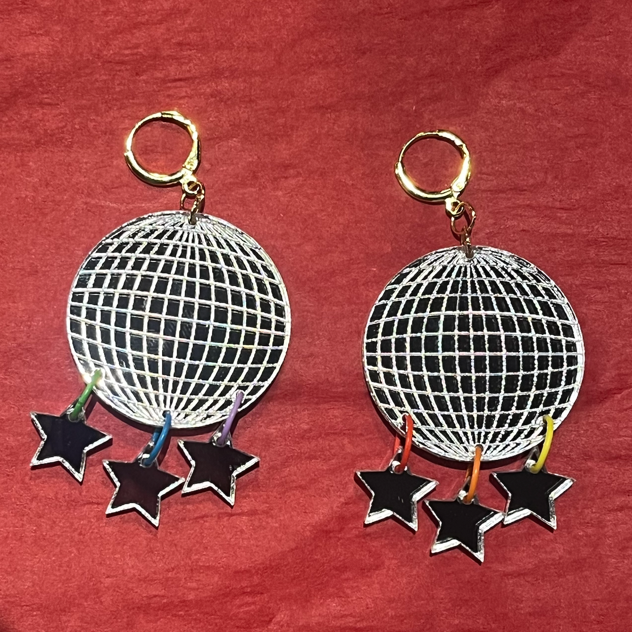 Pair of disco ball earrings with star charms on a red background