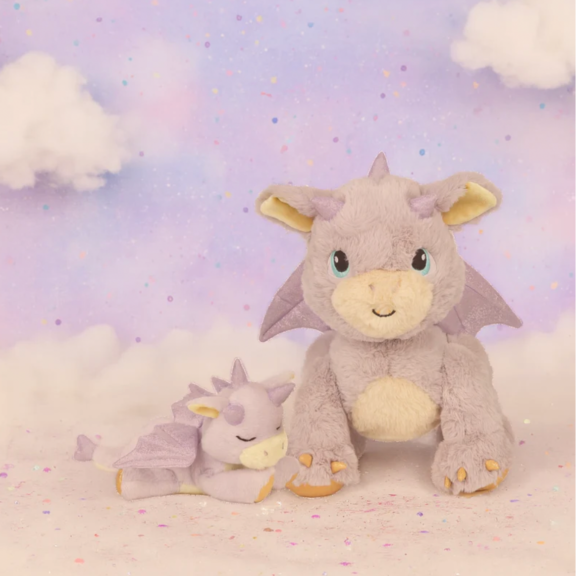 Two dragon plush toys on a soft, cloud-like background with a pastel sky.