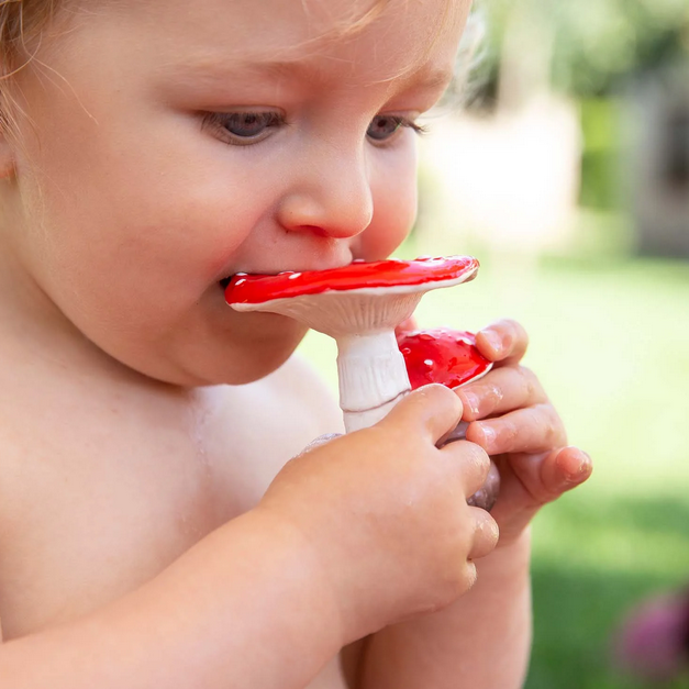 Child using a red and white teether outdoors