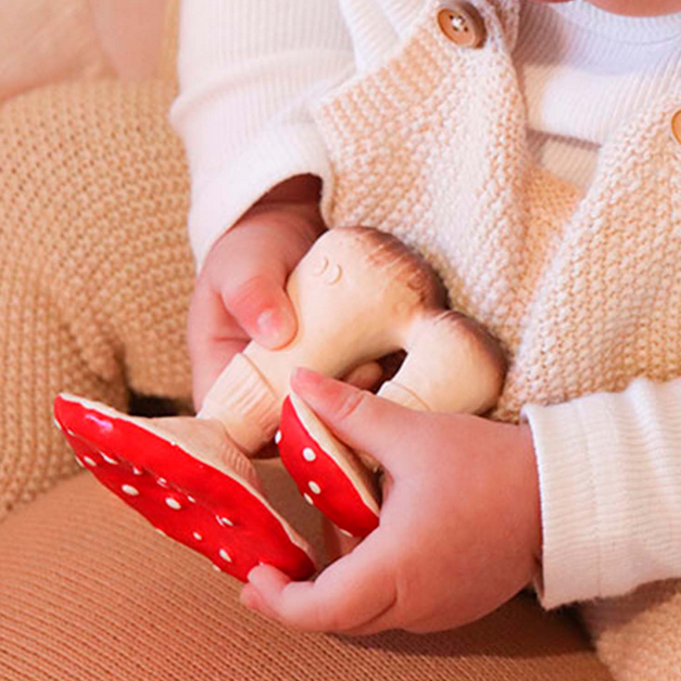 Child holding a rubber toy with red polka dots, wearing a beige knitted sweater.