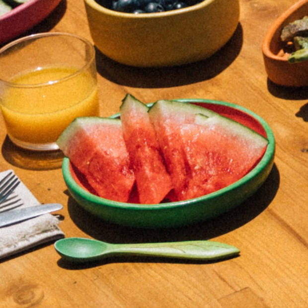 Sliced watermelon in a green bowl on a wooden table with a glass of orange juice.