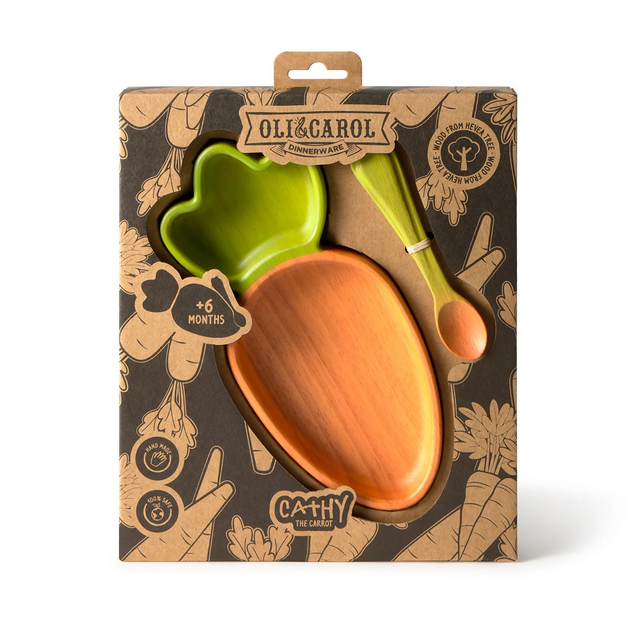 Packaged children's dinnerware set with green bowl, orange plate, and green spoon on a brown patterned background.
