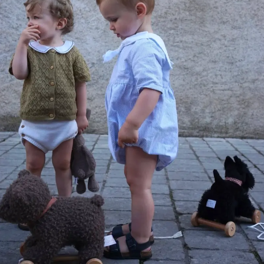 Two children standing outdoors with stuffed animals on a sidewalk.