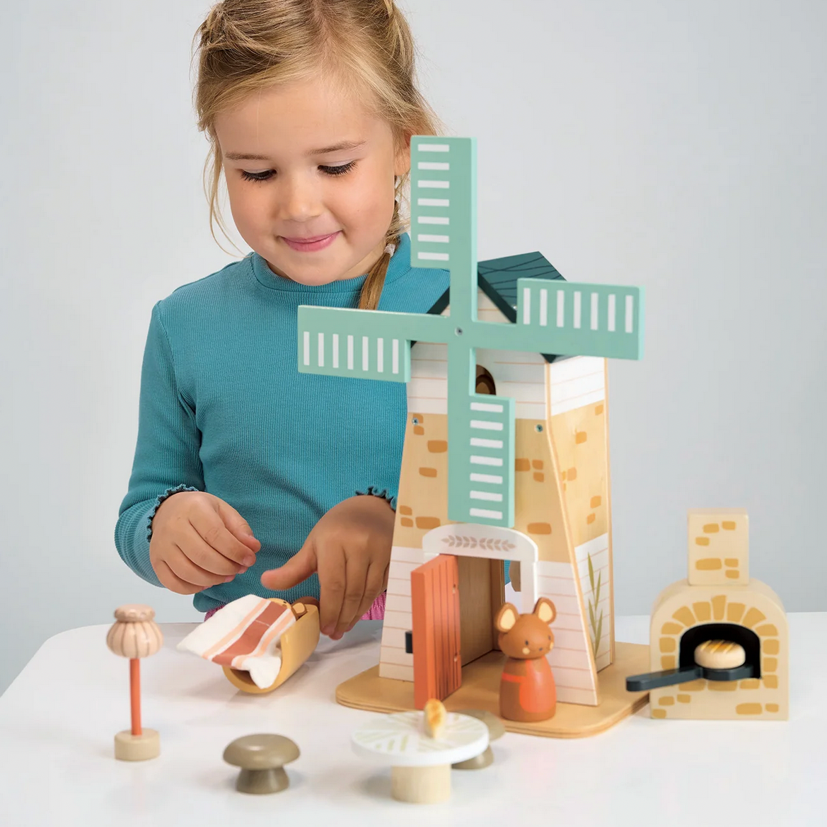 Child playing with a wooden toy windmill set on a white surface.