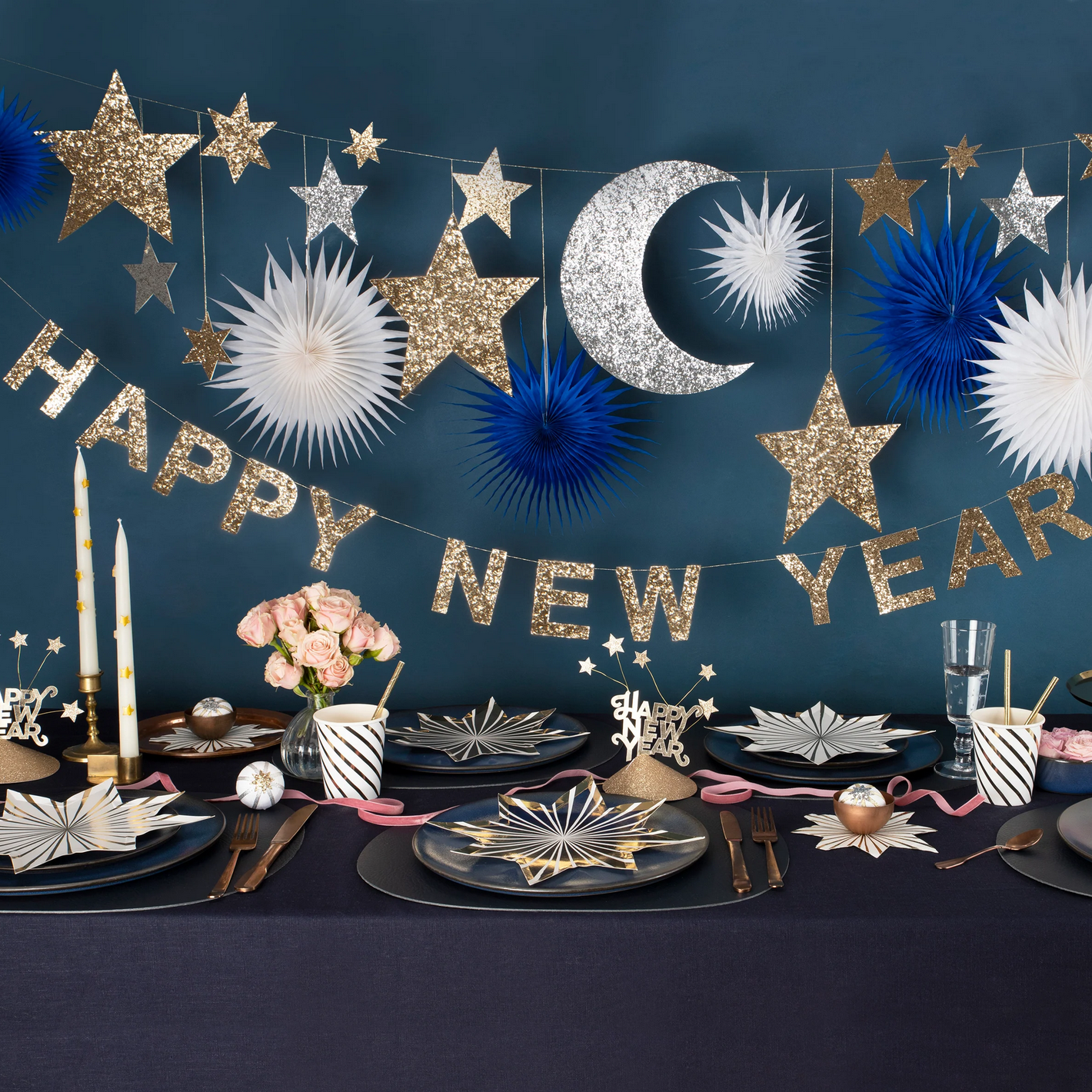 New Year's Eve table setting with decorative garland, plates, and candles against a dark blue background.