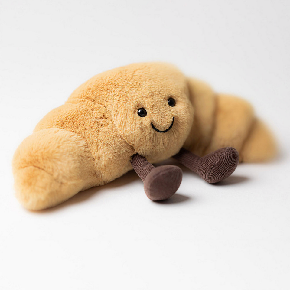 Plush toy resembling a croissant with a smiling face on a white background