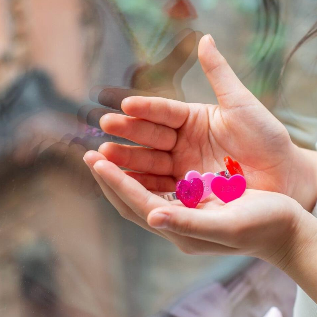 Two small heart-shaped objects held in a person's hands with a blurred background