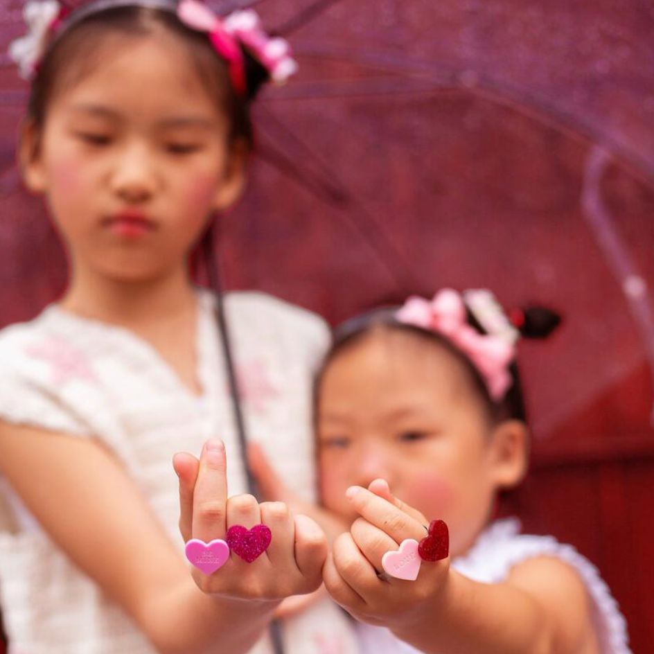 Two young girls with decorative hair bows holding a pink umbrella.