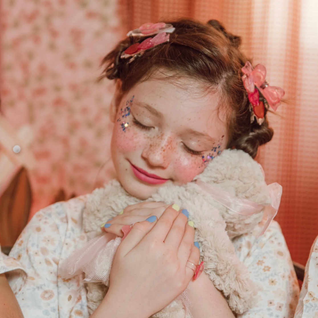 Young girl holding a teddy bear with floral headbands and colorful nail polish.