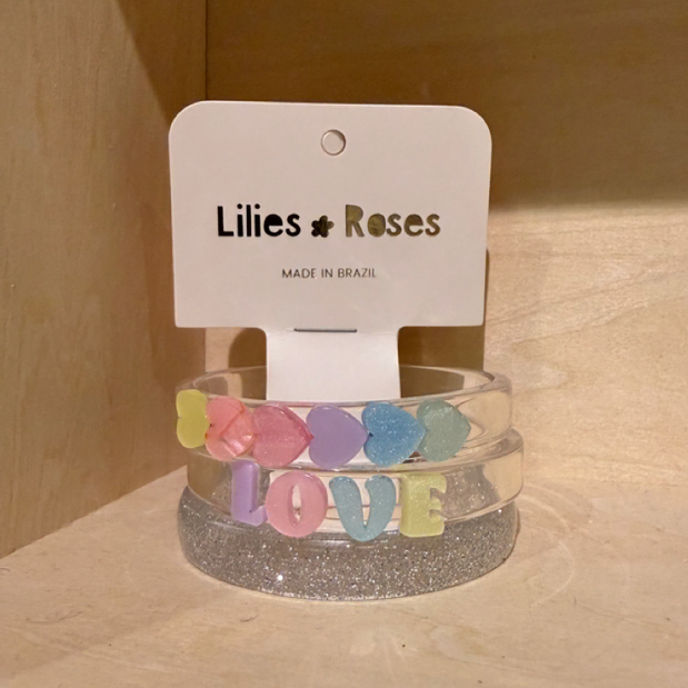 Two clear bracelets with colorful letters on a wooden surface, branded 'Lilies & Roses'.