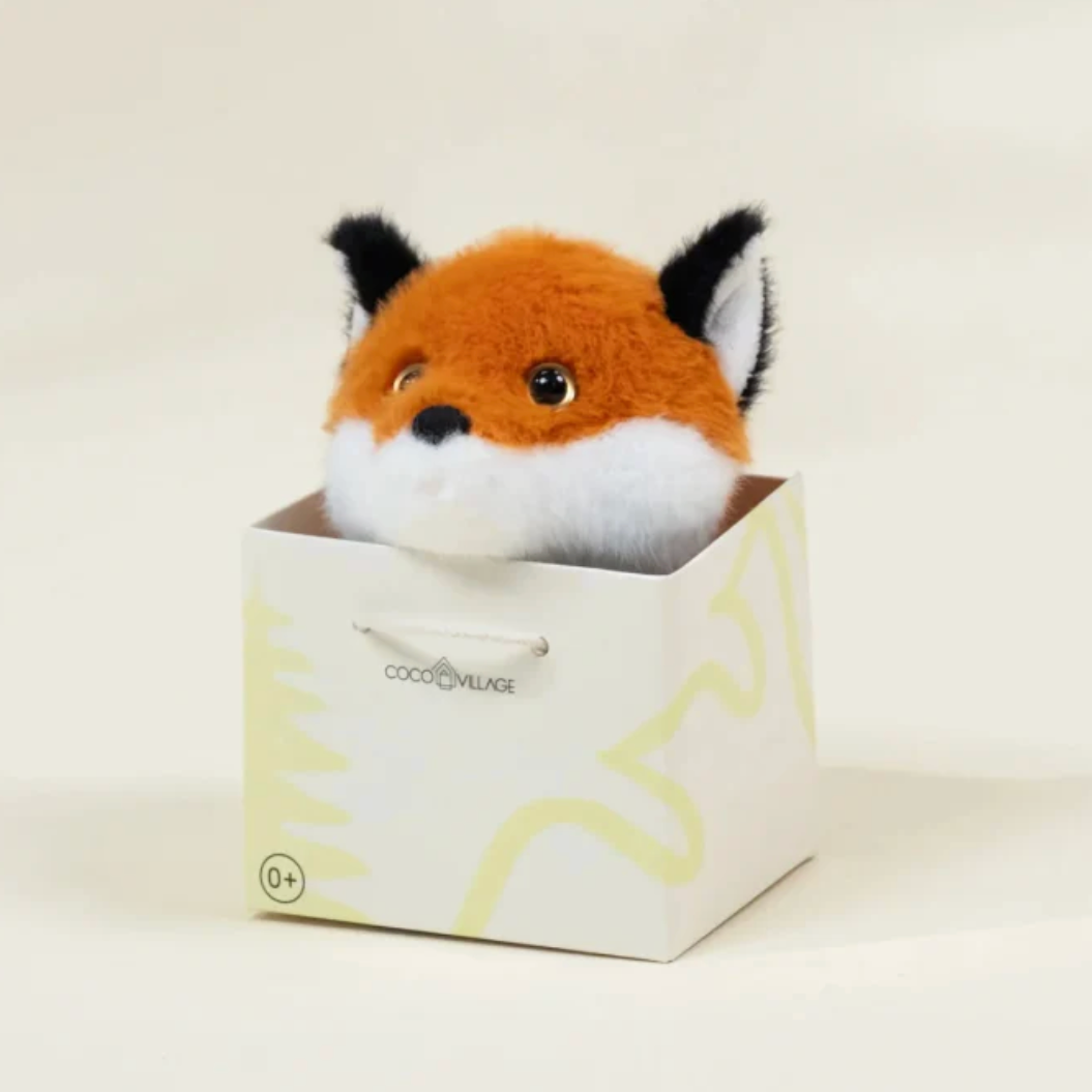 Plush fox toy in a box with a visible brand logo on a light background