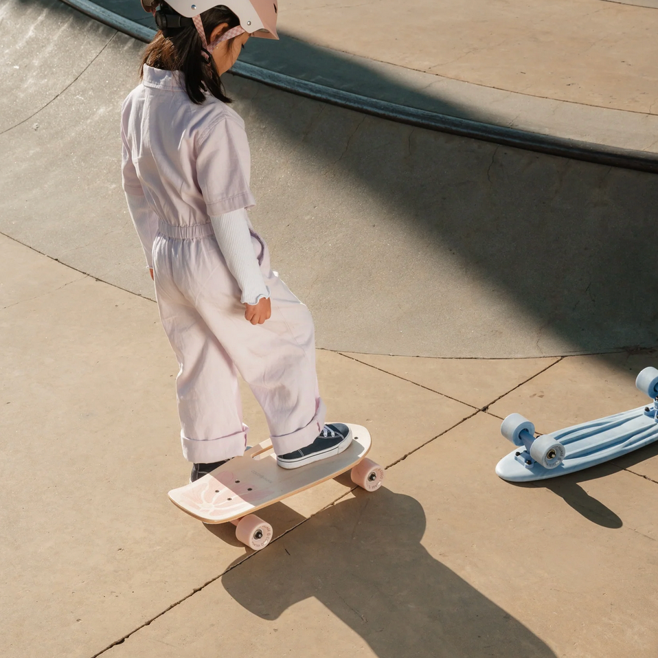 Person in white outfit skateboarding on a concrete surface with another skateboard nearby.