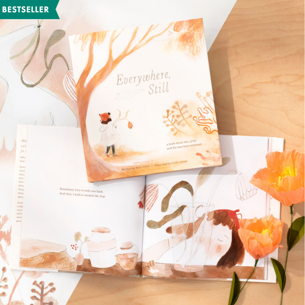 Open book with illustrations and a flower on a wooden surface, labeled as a bestseller.
