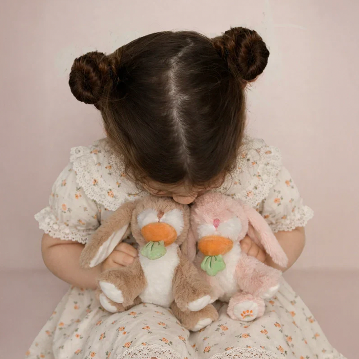 Child holding two plush toys against a plain background