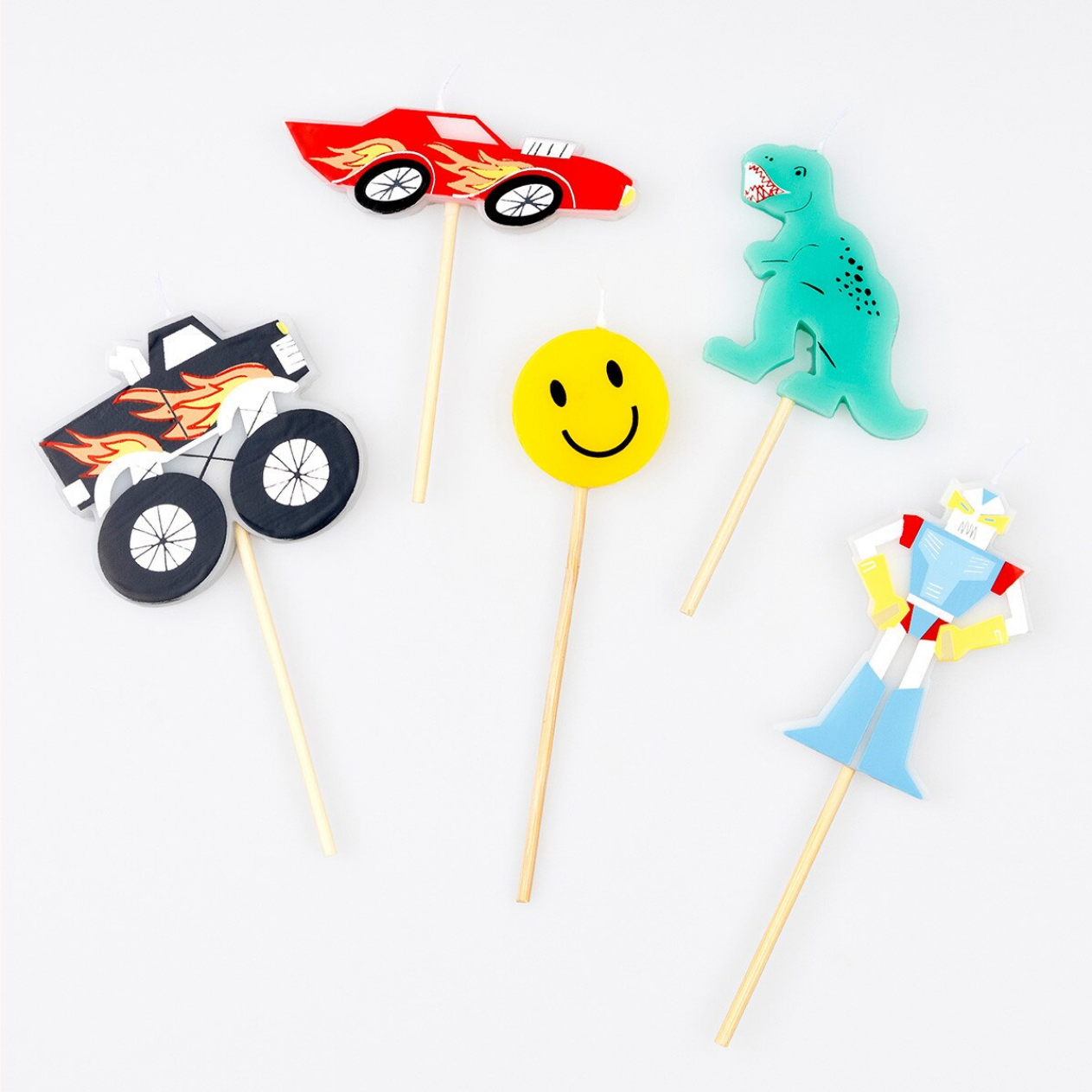 Colorful cupcake toppers shaped like a car, monster truck, smiley face, dinosaur, and clown on sticks against a white background.