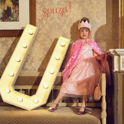 Child in a princess costume standing next to a large letter 'U' with decorative background
