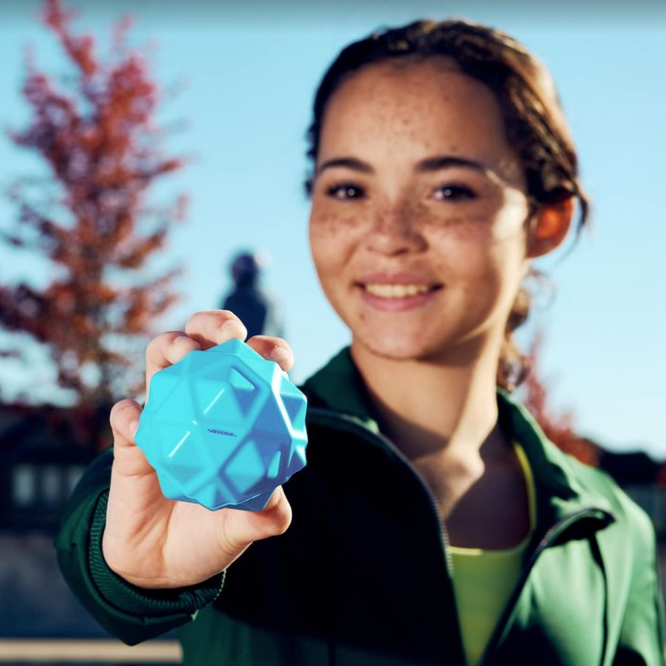 Person holding a blue bouncy ball outdoors with a blurred background