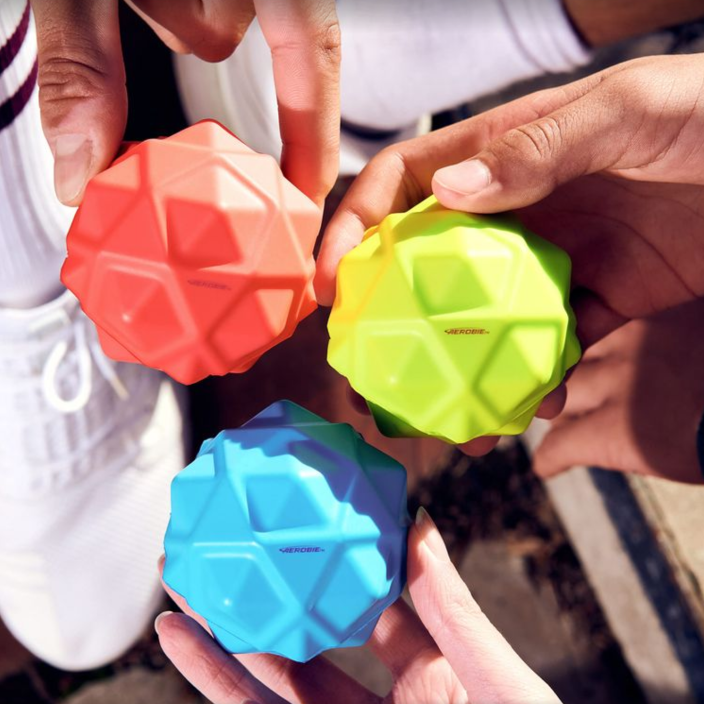 Three colorful geometric balls held by hands against a blurred outdoor background