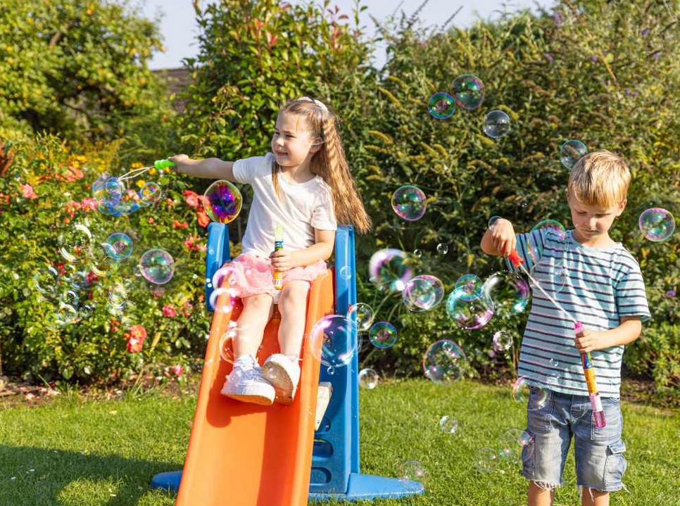 Two children playing with bubble wands on a slide in a garden.