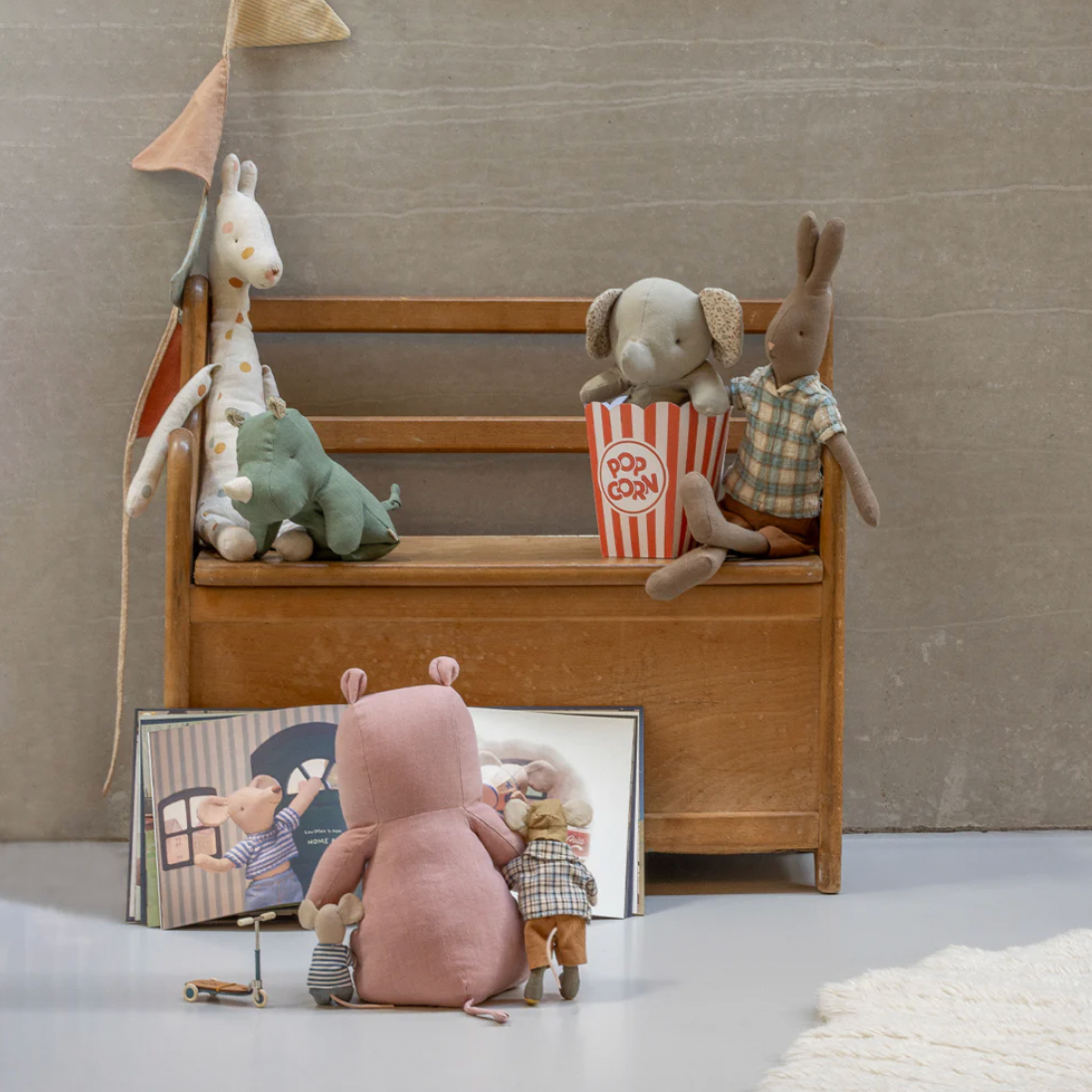 Stuffed animals on a wooden bench with a mirror reflecting a child reading a book.
