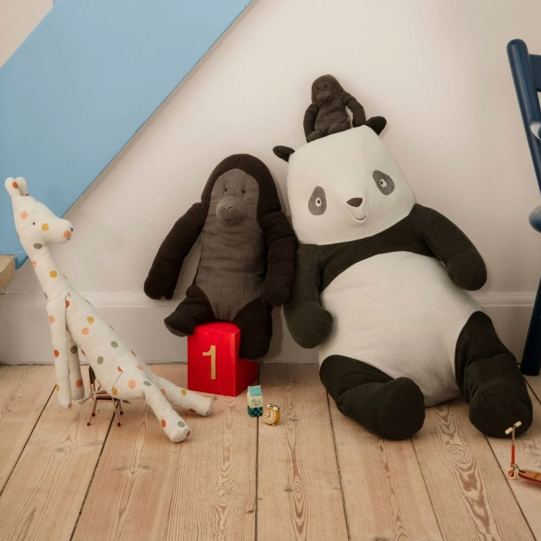 Plush toys including a panda, elephant, and giraffe on a wooden floor with a white wall and blue chair in the background.