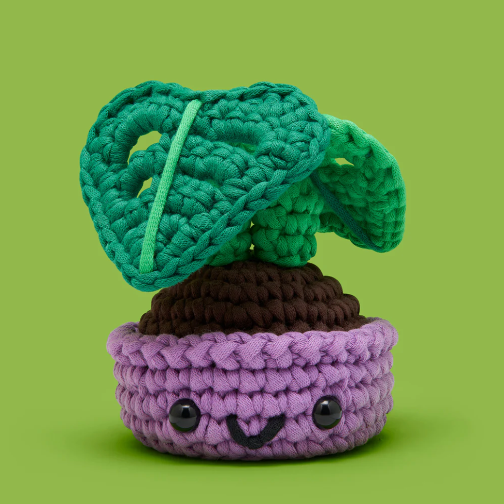 Crocheted plant with a purple pot and green leaves on a green background