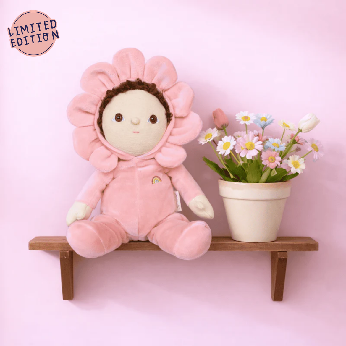 Pink plush toy with flower hat on a wooden shelf with a pink background