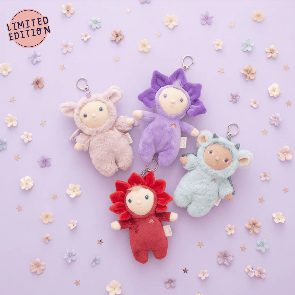 Four colorful plush keychains on a light purple background with flowers.