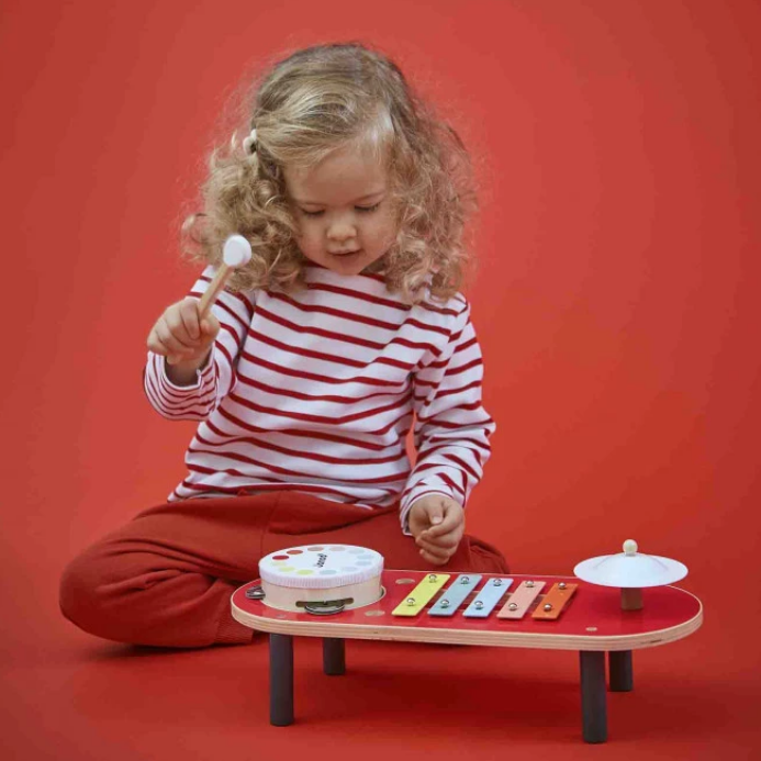Child playing with a toy xylophone on a red background