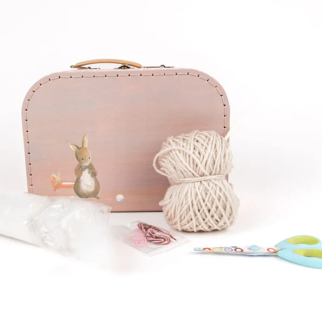 Pink suitcase with a rabbit design, yarn ball, and scissors on a white surface.