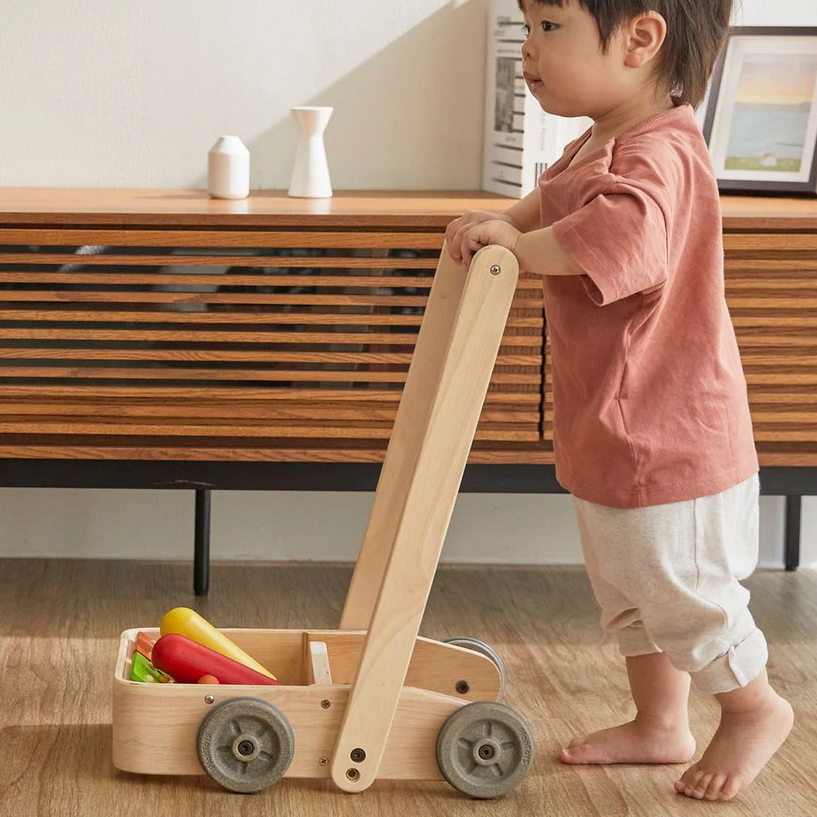 Child playing with a wooden toy cart on a wooden floor.