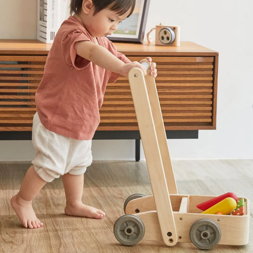 Child playing with a wooden toy cart on a wooden floor.