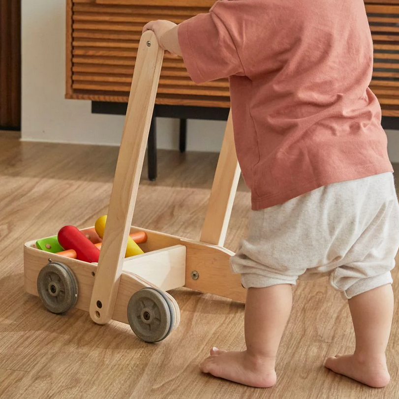 Child pushing a wooden cart with toys on a wooden floor